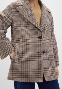 Rutig kavaj i ullblandning med bruna, blå och krämfärgade mönster; har en bred krage, två knappar och sidofickor.