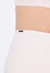 Fascia seamless color beige chiaro con un piccolo etichetta nera logo. Il materiale sembra liscio ed elasticizzato, progettato per comfort e vestibilità.