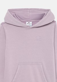 Lys lavendel hettegenser laget av mykt stoff, med en frontlomme, mansjetter på ermene og en preget logo på brystet.