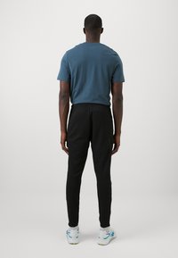 Mørkeblå bomull t-skjorte og svarte treningsbukser, sett fra baksiden. Buksene har elastisk midje og tapered ben. Hvite joggesko.