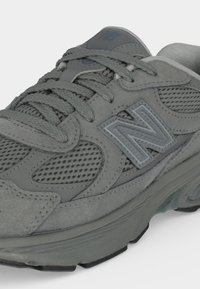 Baskets grises New Balance avec panneaux en mesh et en daim, lacets épais et logo en relief "N" sur le côté.