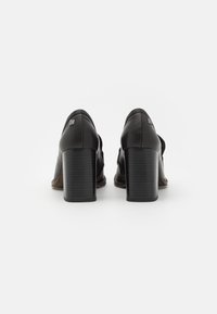 Černé kožené lodičky na vysokém podpatku se štíhlým designem, s texturovaným blokovým podpatkem a jemným logem na zadní straně.