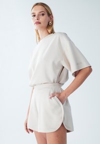 Beige top med korte ærmer og matchende shorts lavet af blødt stof, med en afslappet pasform, elastisk talje og sidelommer.