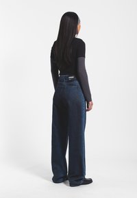 Jeans de denim oscuros de tiro alto con un corte holgado, que cuentan con un diseño clásico de bolsillo trasero y una etiqueta en la cintura.