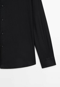 Chemise noire à manches longues boutonnée, vue de face, mettant en valeur les boutons, le poignet et le tissu lisse sur un fond blanc uni.