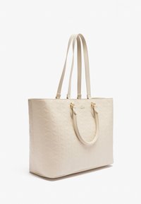 Sac fourre-tout beige matelassé avec deux longues anses et des accessoires en ton or. Texture lisse avec un motif géométrique sur la surface.