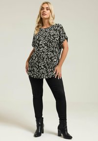 Czarny i biały wzorzysty top z krótkim rękawem, zestawiony z czarnymi rurkami i czarnymi botkami na obcasie. Gładka tkanina i luźny krój.