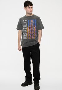Grey graphic t-shirt featuring multicolored skeleton design, paired with black pants and black boots, set against a plain white background.