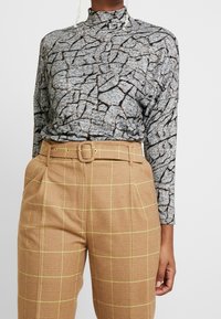 Top de manga larga en gris con un patrón agrietado, combinado con pantalones de cuadros marrones de cintura alta con cinturón y detalles amarillos.
