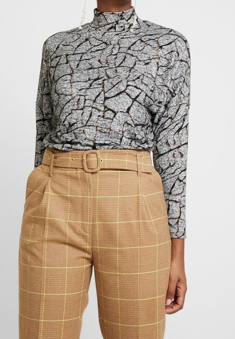 Top de manga larga en gris con un patrón agrietado, combinado con pantalones de cuadros marrones de cintura alta con cinturón y detalles amarillos.