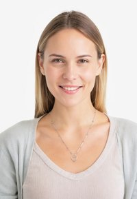 Sølv halskæde med et hjertevedhæng og små runde perler, båret med en lysegrå cardigan over en lys beige top. Glat tekstur.