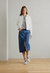White denim jacket, gray top, blue denim skirt with a front slit, and gray sneakers on a wooden floor against a plain wall.