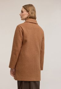 Brązowy, teksturowany płaszcz wełniany z kołnierzem, długimi rękawami, prostym krojem i długością do połowy uda, z subtelnym wzorem i bez widocznych zapięć.
