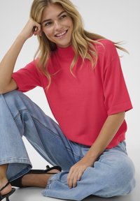 Bright red, short-sleeve mock neck top paired with wide-leg light blue jeans and black heeled sandals, showcasing a relaxed style.