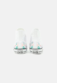 Białe wysokie trampki Converse z kwiatowym wzorem w różowym i zielonym na podeszwie, czarnym logo oraz teksturowanym materiałem z płótna.