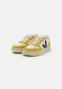 Yellow and white sneakers with suede and leather materials. Perforated toe, beige laces, dark logo accent, and rubber sole.