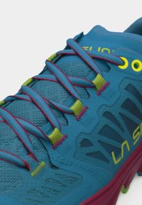 Chaussure de sport La Sportiva bleue et rouge avec œillets jaunes et passants à lacets, présentant une tige détaillée en maille et matériaux synthétiques avec les lacets noués.
