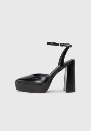 Chaussure à talon haut plateforme noire avec bride à la cheville et talon bloc épais sur fond clair uni.