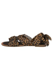 Sandalias planas con estampado de leopardo, con tiras de tela atadas, suela marrón y una textura suave. Diseño abierto en la parte delantera y un ajuste relajado.