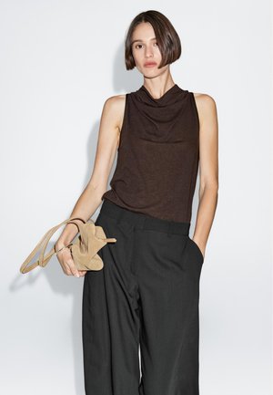 Bruine mouwloze top met gedrapeerde halslijn, gecombineerd met losse zwarte broek en een paar tan hoge hakken. Glad materiaal, neutrale tinten.