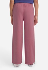 Ružičaste široke hlače izrađene od mekog materijala, s elastičnom gumom u struku i bočnim džepovima. U kombinaciji s bijelim Converse tenisicama.