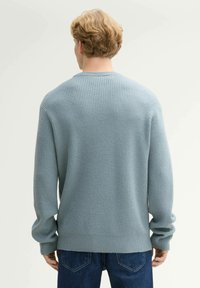 Jasnoniebieski sweter o teksturowym wykończeniu z okrągłym dekoltem, ściągaczami przy rękawach i u dołu. Wzór w waflowy splot, z opadającymi ramionami i luźnym krojem.