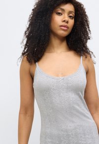 Camisole grise sans manches avec un délicat bord en dentelle, des motifs tricotés verticaux et un petit nœud décoratif au niveau de l'encolure. Texture douce.