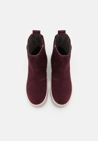 Paire de bottines en daim rouge foncé avec des semelles blanches, vues de dessus, montrant la doublure intérieure et les fermetures éclair latérales.