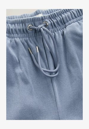 Pantaloni de trening bleu deschis, cu un material texturat, având un brâu elastic și un șnur cu ochiuri argintii și vârfuri metalice.
