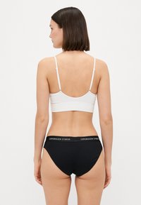 Svart bomullstruse med hvit elastisk midjebånd med teksten "Copenhagen Studios"; kombinert med en hvit ribbestrikket bralette.