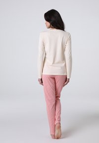 Camicia a maniche lunghe color crema abbinata a pantaloni da pigiama a righe rosa, realizzati in tessuto morbido, con un design aderente e una silhouette snella.