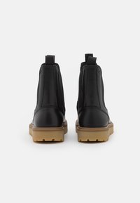 Bottes chelsea en cuir noir avec des panneaux élastiques sur les côtés et des poignées de tirage. Comprend une semelle en caoutchouc marron texturé pour une meilleure adhérence. Construction robuste.
