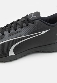 Zwarte sportieve schoen met een gestructureerd oppervlak, zilveren accenten en zes spikervormen voor grip op een vlakke zool. Voorzien van ronde veter en een gevoerde kraag.