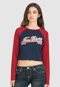 Langärmliges Crop-Top mit navyfarbenem Körper und roten Raglanärmeln. Verfügt über das weiße "True Religion"-Logo und "02" in kontrastierendes Design. Aus Baumwollmaterial.