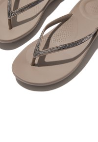 Beige flip-flops met een gestructureerde zool en dunne bandjes versierd met kleine, glinsterende strassteentjes langs de bovenrand.