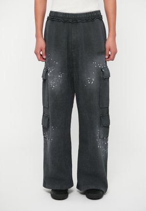 Laza illeszkedésű cargo nadrág, sötétszürke anyagból, több zsebbel és fehér spriccelő mintával. Rugalmas derékpánt.