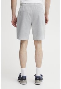 Shorts de sport gris avec une ceinture élastique, un ourlet plat et deux poches arrière. Tissu texturé, associés à des chaussures de sport bleu marine et des chaussettes blanches.