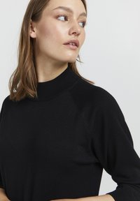 Črn pulover s visokim ovratnikom in raglan rokavi. Mehka, lahka tkanina z gladko teksturo. Minimalističen dizajn brez vzorcev.