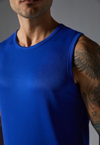 Top desportivo azul, feito de um tecido suave e elástico; apresenta um decote redondo e um design sem mangas com uma silhueta ajustada.