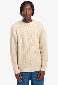 Beige gebreide trui met kabelpatroon en geribbelde zoom. Met een ronde halslijn en lange mouwen, gemaakt van gestructureerd garen.