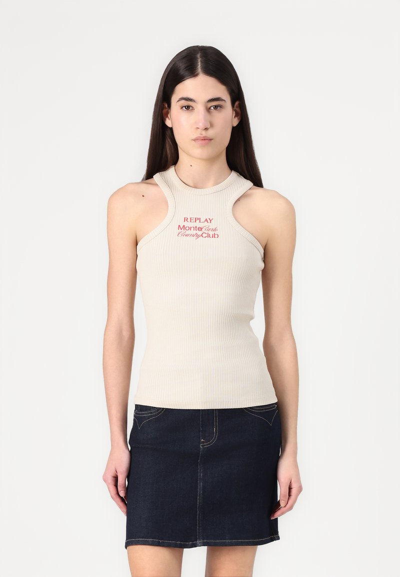 Beige geribbelde mouwloze top met een hoge nek en uitsnijdingen op de schouders, met in het rood gedrukt de tekst "REPLAY Monte Carlo Country Club."