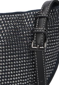 Zwarte leren schouderriem met zilveren hardware bevestigd aan een gestructureerde donkerblauwe stof versierd met kleine, glanzende, ronde rhinestones.