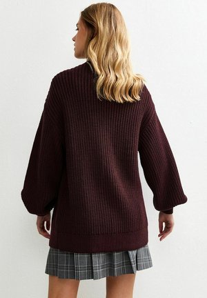 Burgundy oversized knit sweater with textured fabric and wide sleeves, paired with a gray plaid mini skirt.