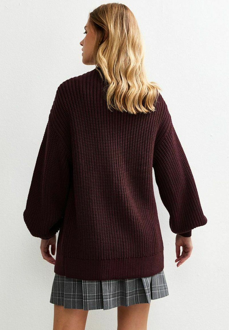 Burgundy oversized knit sweater with textured fabric and wide sleeves, paired with a gray plaid mini skirt.
