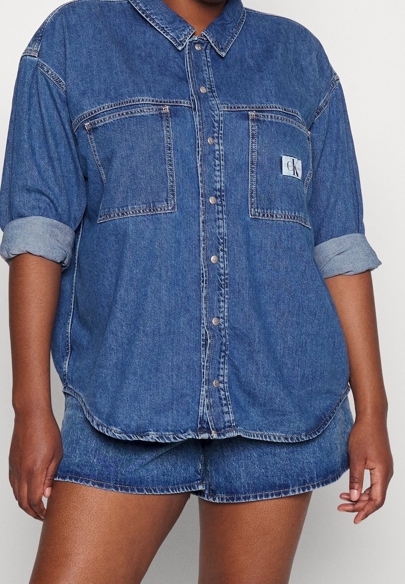 Denimskjorta, ljusblå, med knäppning fram, två bröstfickor, uppvikta ärmar och CK-logotyp. Matchas med passande denimshorts.