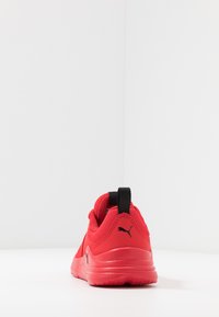 Baskets de sport rouges avec une tige en tissu texturé, un col rembourré, un logo noir au talon et une semelle en caoutchouc texturé.