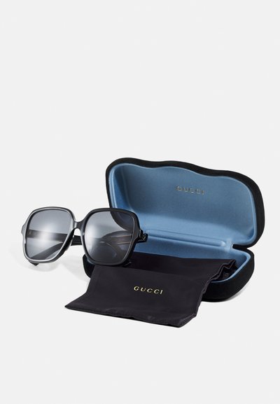 Lunettes de soleil Gucci avec de grandes montures carrées noires, verres gris, présentées dans un étui noir doux avec un intérieur bleu et un logo. Comprend un chiffon de nettoyage.
