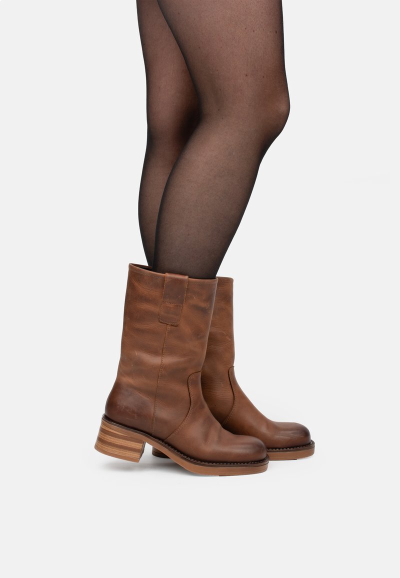 Braune Lederstiefel bis zur Wade mit glatter Oberfläche, ausgestattet mit einem gestapelten Absatz und seitlichen Ziehschlaufen zum einfachen Anziehen.