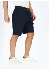 Navy blue shorts made of cotton, featuring a woven belt, side pockets, and a straight cut. Paired with white sneakers with black accents.