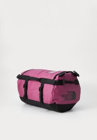 Rózsaszín duffel táska fekete részletekkel, tartós anyagból készült. Állítható vállpántokkal, oldalsó fogantyúkkal és egy jól látható logóval rendelkezik.